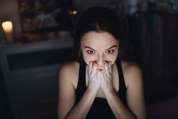 Scared and worried young girl with laptop sitting indoors, internet abuse concept.